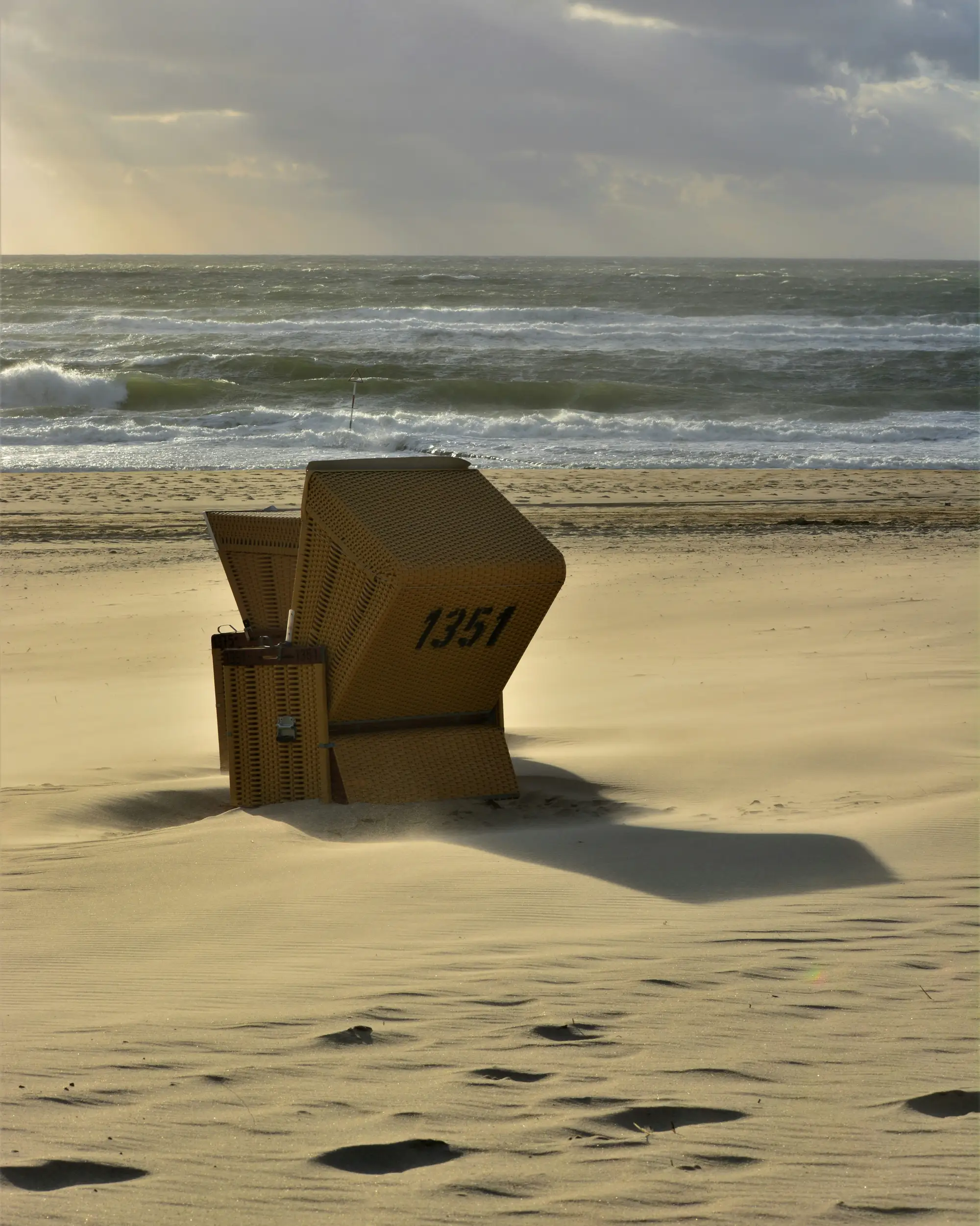 Ein Strandkorb im wehenden Sand vor der Ostseebrandung